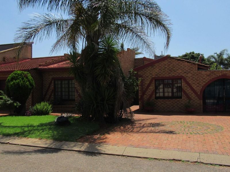 Front view of a face-brick house featuring a paved driveway, tiled roof, and secure gated entrance.