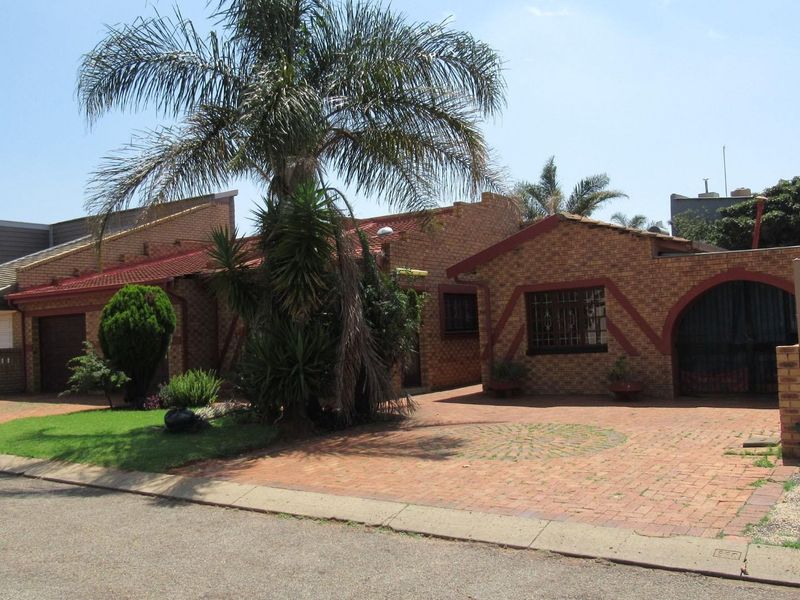 Front view of a face brick house featuring a paved driveway, security features, and established garden elements.
