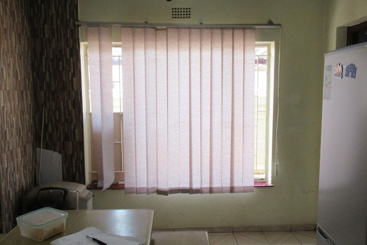 A kitchen area featuring tiled flooring, textured wall accents, and a window fitted with vertical blinds.