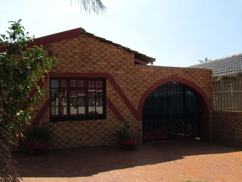Front exterior view of a face brick house featuring an arched gate, security window bars, and a paved driveway.