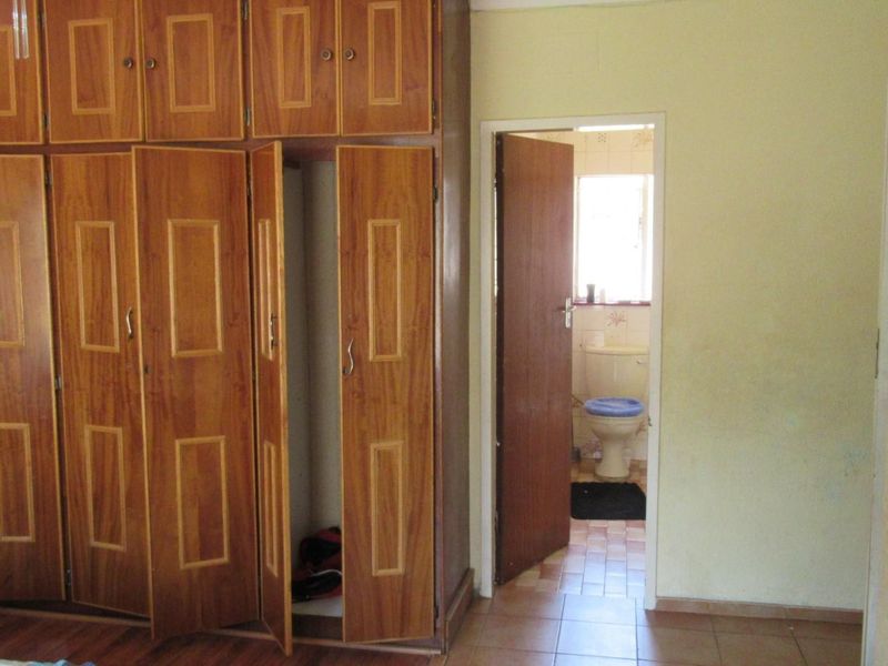 A bedroom featuring built-in wooden cupboards and tiled flooring, with an adjacent view into a bathroom.