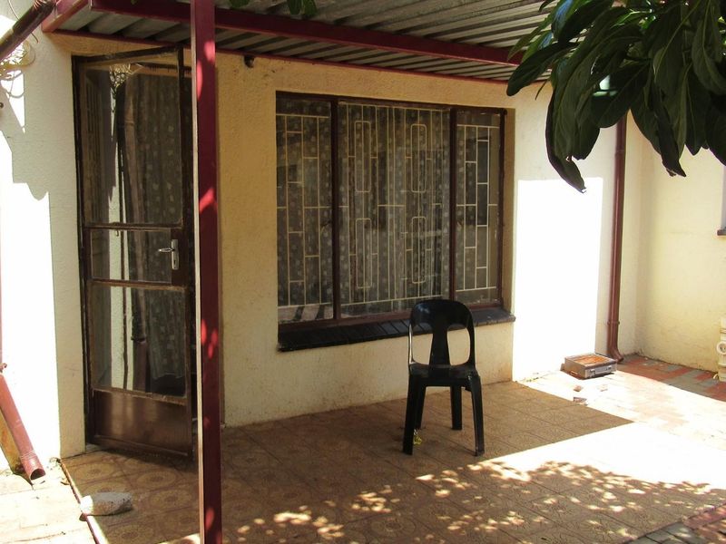 A covered outdoor patio area featuring tiled flooring, metal support structures, and security-fitted windows and doors, requiring some maintenance and cosmetic updates.