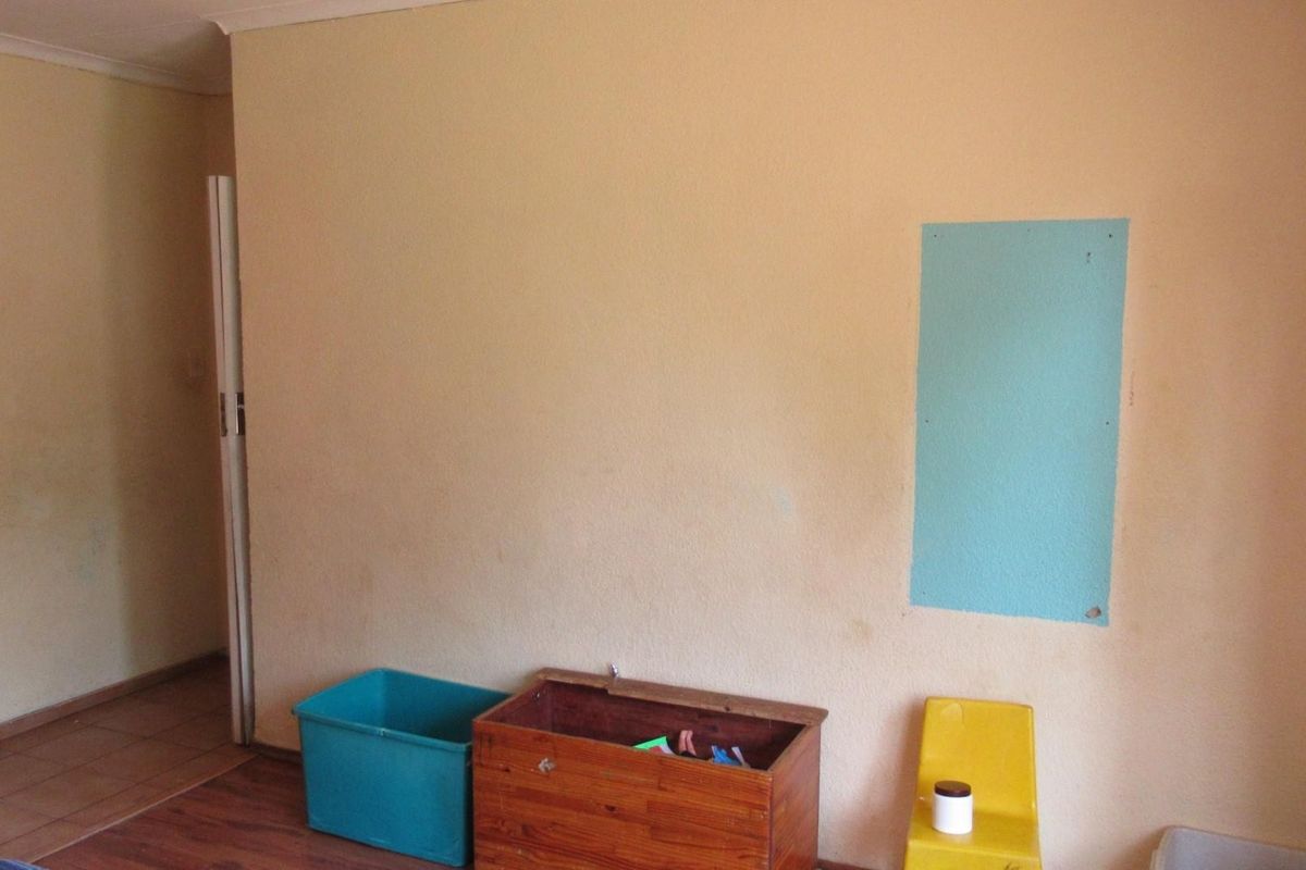 A sparsely furnished living area featuring laminate flooring and plain walls with visible surface imperfections.