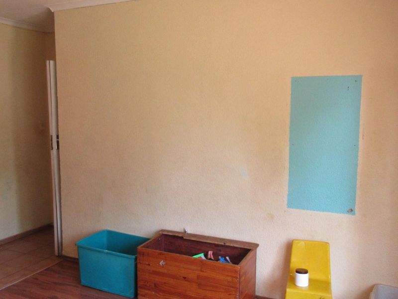A sparsely furnished living area featuring laminate flooring and plain walls with visible surface imperfections.