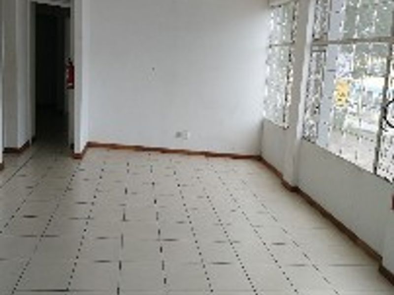 An empty, open-plan office space featuring tiled flooring and large windows with security bars, offering a blank canvas for professional use.