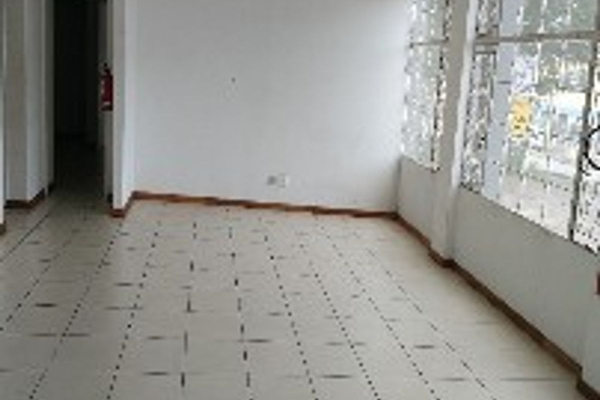 An empty, open-plan office space featuring tiled flooring and large windows with security bars, offering a blank canvas for professional use.