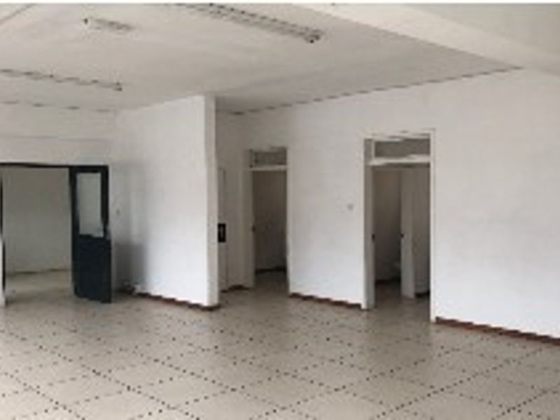 An empty, open-plan office space featuring tiled flooring and fluorescent lighting, offering a blank canvas for professional customization.