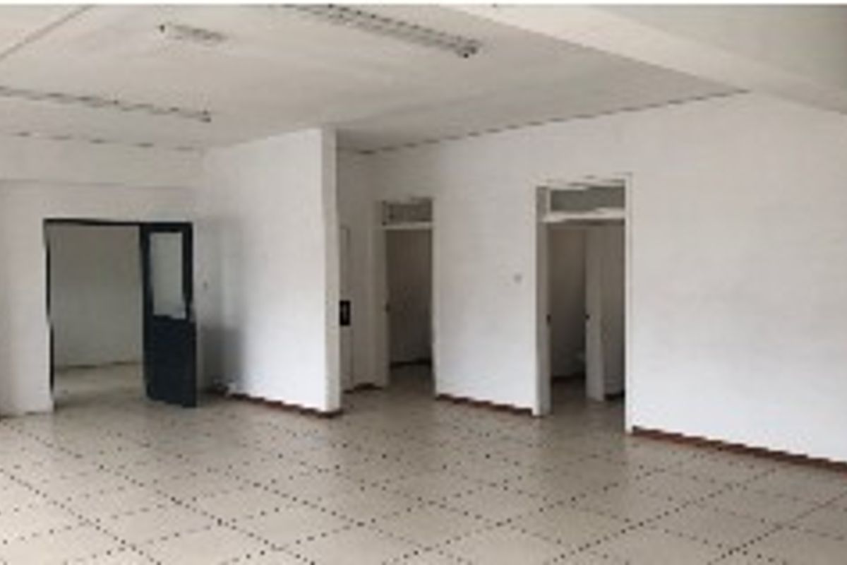 An empty, open-plan office space featuring tiled flooring and fluorescent lighting, offering a blank canvas for professional customization.