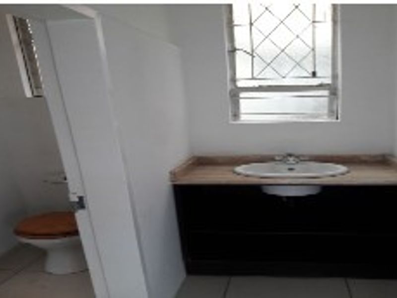A functional bathroom featuring a vanity cabinet with a basin and a separate toilet area with security bars on the window.