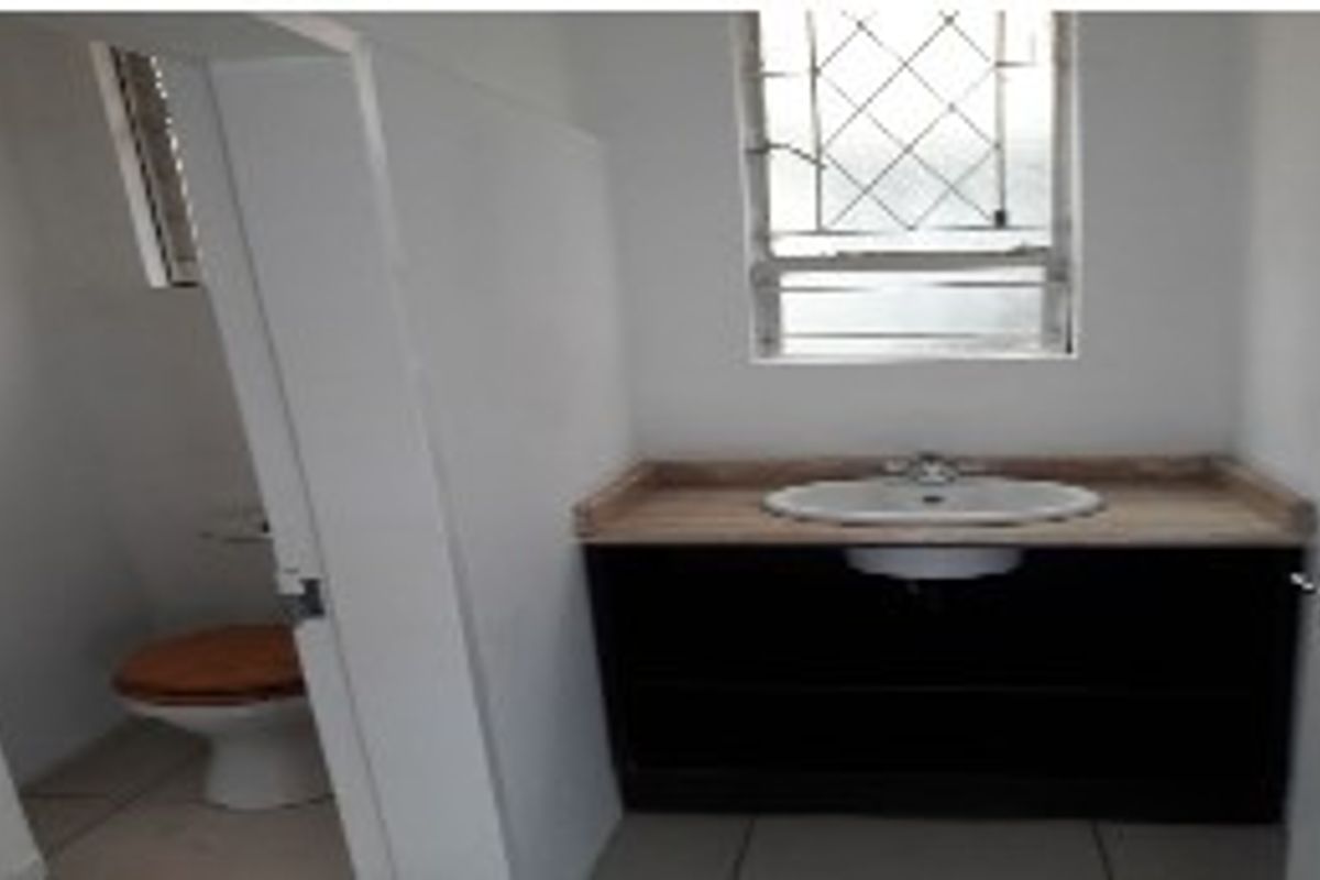 A functional bathroom featuring a vanity cabinet with a basin and a separate toilet area with security bars on the window.