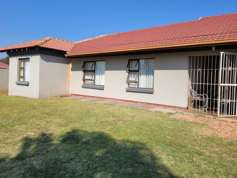 Rear view of the house featuring a well-maintained lawn, terracotta tiled roof, and secure entrance with metal security gate.