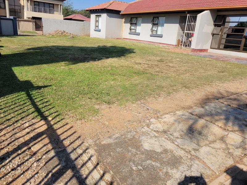 Rear view of the property featuring a lawn area, paved section, and security-fitted windows and doors.