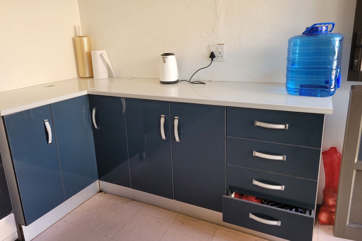A functional kitchen corner featuring glossy blue cabinetry, white laminate countertops, and tiled flooring, providing practical storage and workspace.