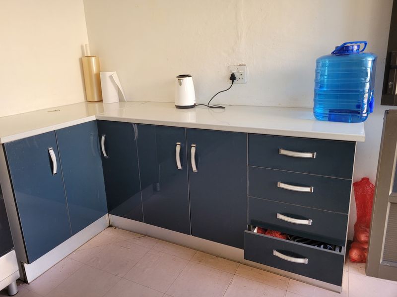 A functional kitchen corner featuring glossy blue cabinetry, white laminate countertops, and tiled flooring, providing practical storage and workspace.