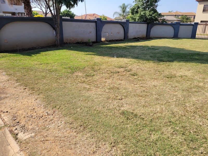 A spacious backyard garden featuring a large lawn area enclosed by a perimeter wall with decorative architectural detailing.