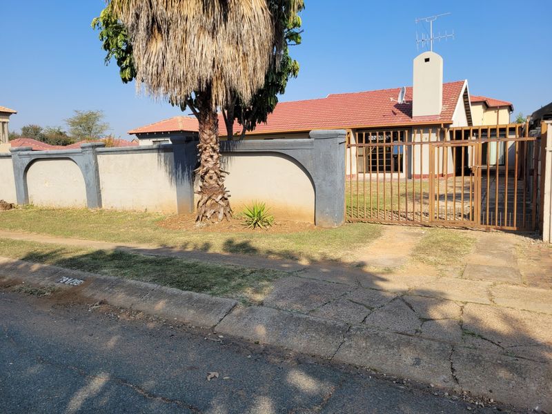 Front view of a residential property featuring a tiled roof, chimney, and a gated perimeter wall with a paved driveway entrance.