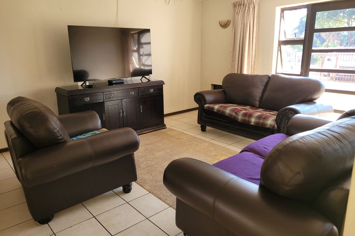 A living room featuring tiled flooring, coved ceilings, and large top-hung windows providing natural light.