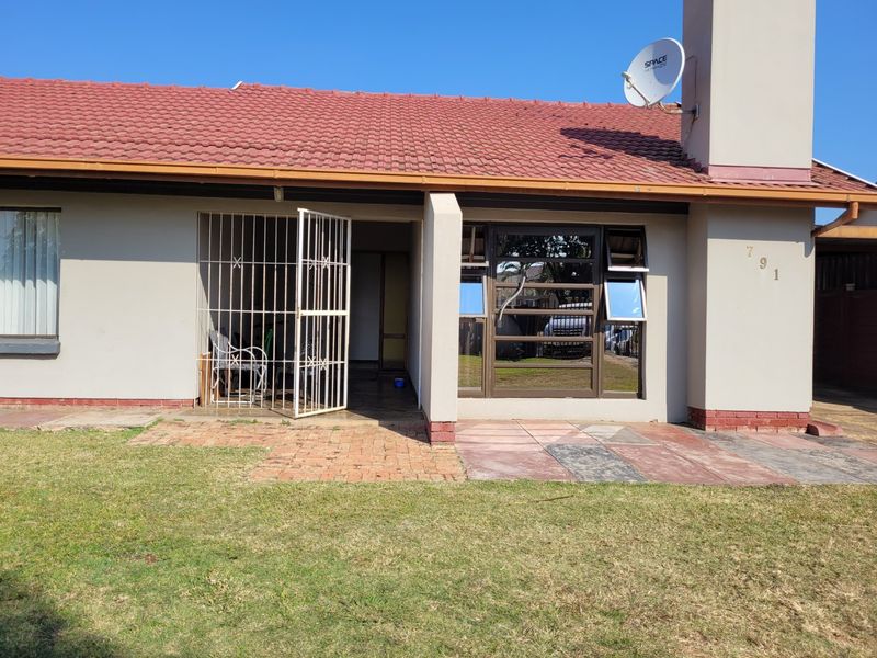 Rear exterior view of the house featuring a tiled roof, brick chimney, paved patio area, and secure entrance with a metal security gate.