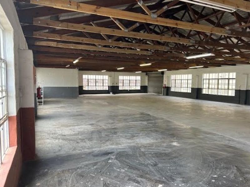 Spacious open-plan office area featuring exposed timber roof trusses, industrial steel-framed windows, and durable concrete flooring, suitable for a versatile workspace.