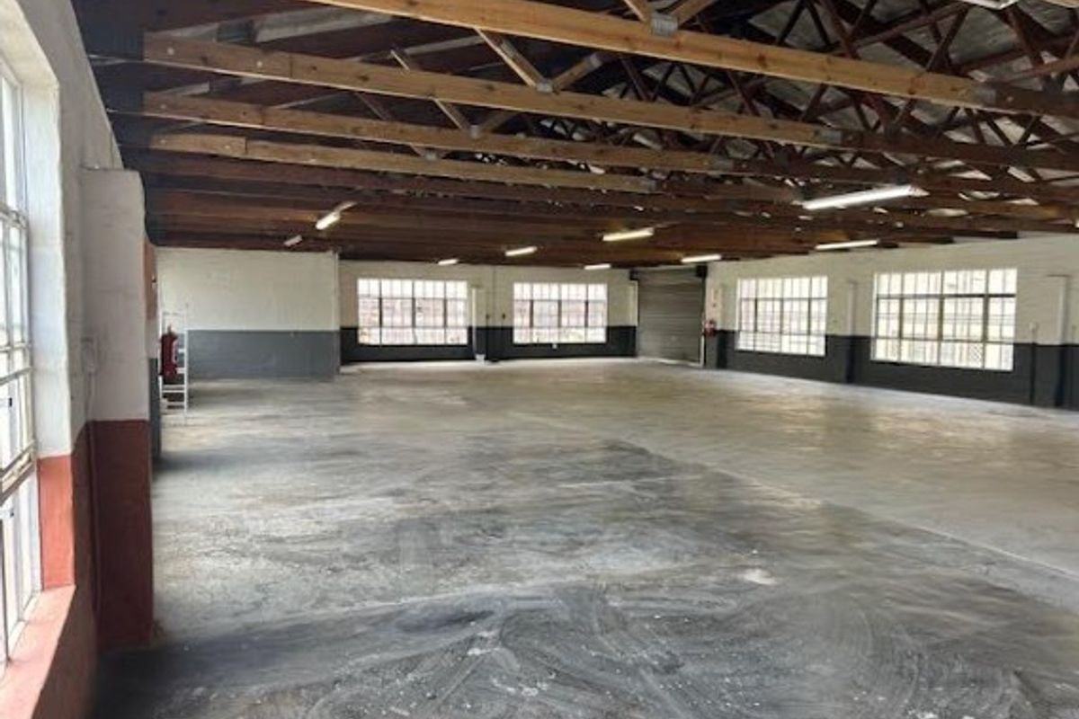 Spacious open-plan office area featuring exposed timber roof trusses, industrial steel-framed windows, and durable concrete flooring, suitable for a versatile workspace.