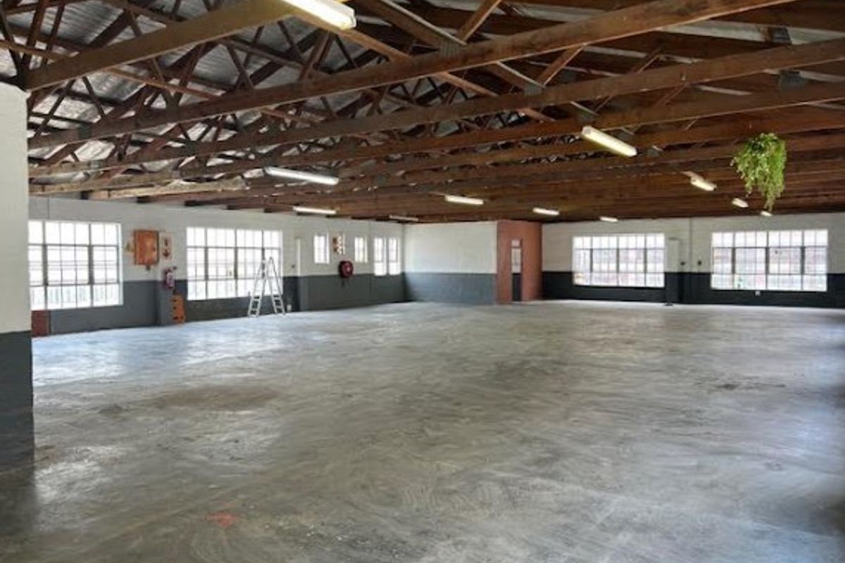 Spacious open-plan office area featuring exposed timber roof trusses, industrial steel-framed windows, and polished concrete flooring in a versatile commercial setting.