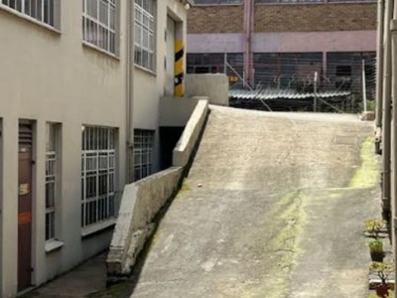 Rear exterior view of an industrial office building featuring a concrete access ramp, steel-framed windows, and weathered exterior surfaces.