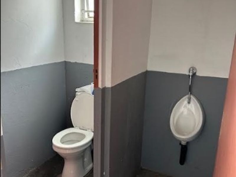 A basic office restroom facility featuring a standard toilet and wall-mounted urinal with concrete flooring and ventilation block detailing.