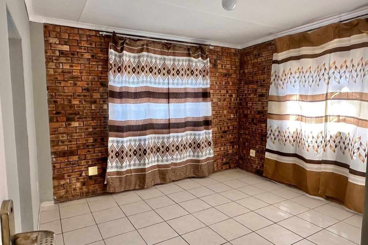 An empty living room featuring exposed brick walls and neutral ceramic floor tiles, offering a blank canvas for interior design.