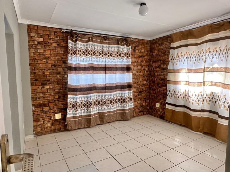 An empty living room featuring exposed brick walls and neutral ceramic floor tiles, offering a blank canvas for interior design.