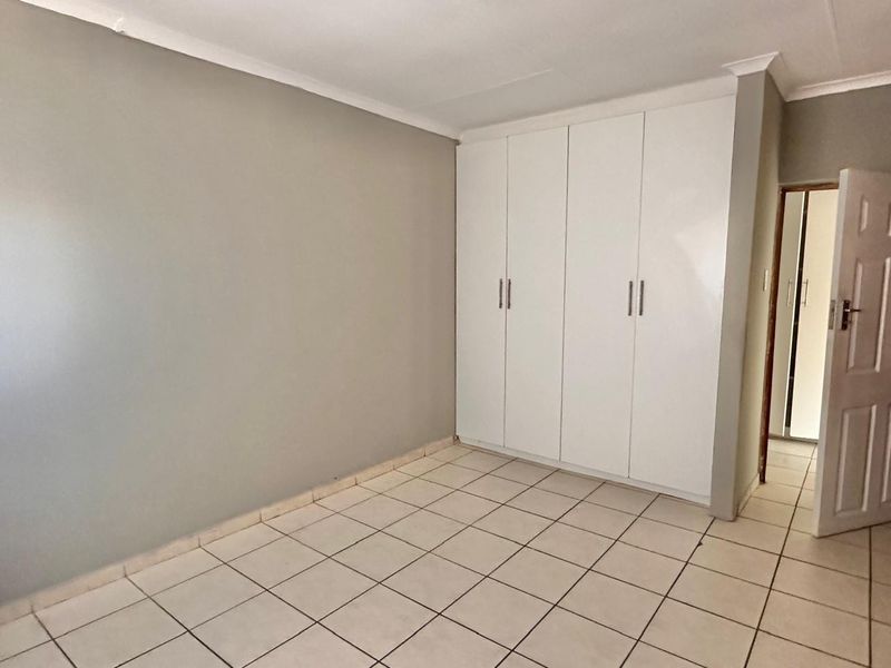 A clean, empty bedroom featuring neutral wall paint, white built-in cupboards, and tiled flooring, offering a blank canvas for personalization.