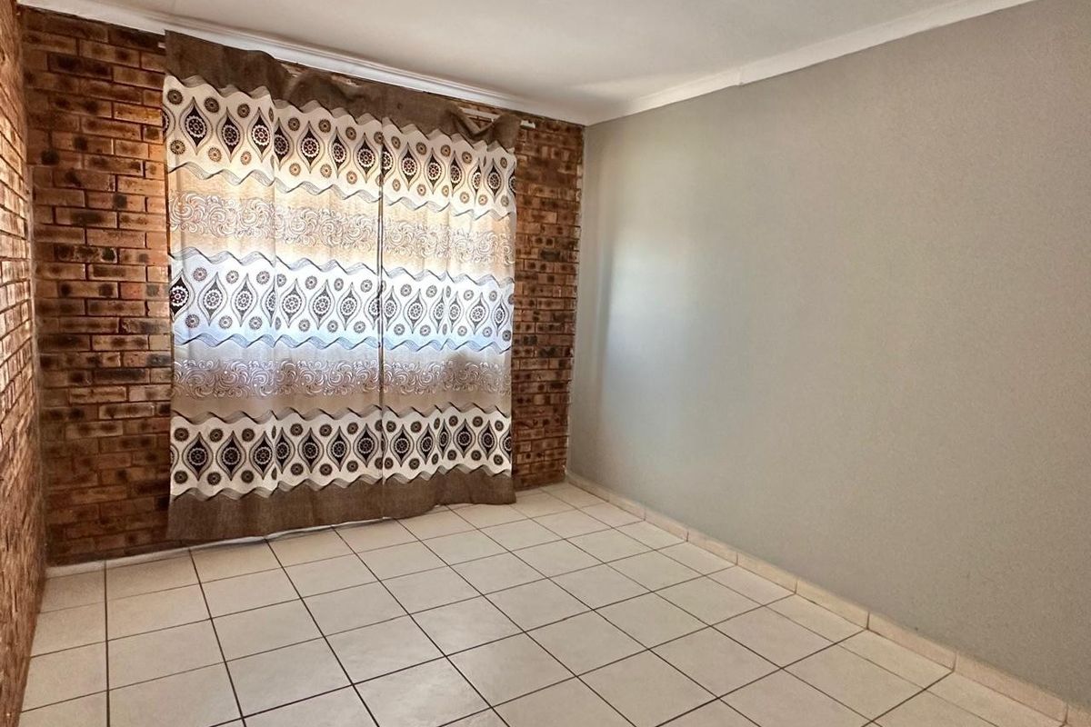 A bright, empty bedroom featuring an exposed brick feature wall, neutral painted walls, and durable ceramic floor tiles.