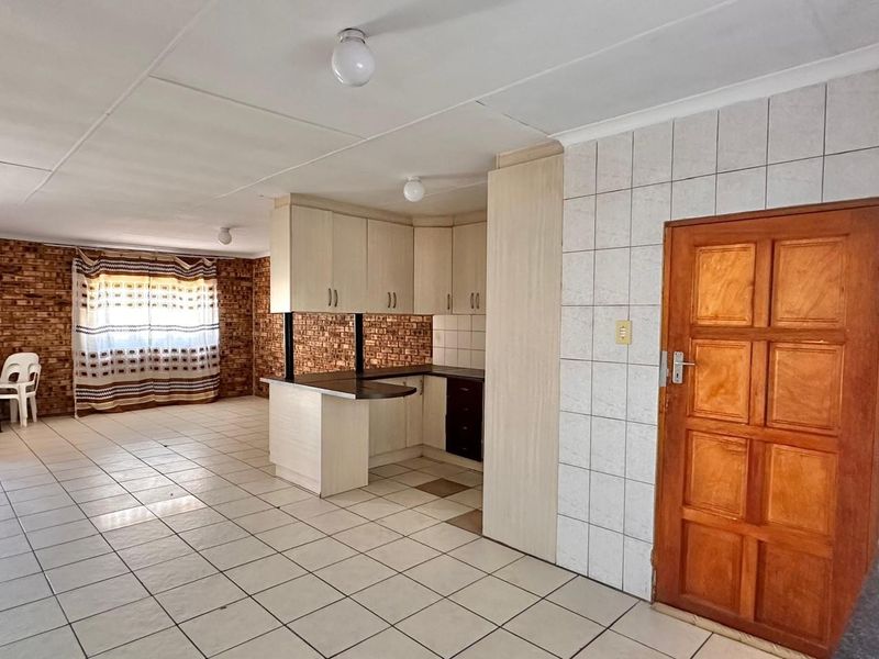 Open-plan living and kitchen area featuring tiled flooring, an exposed brick wall, and built-in cabinetry with a breakfast bar.