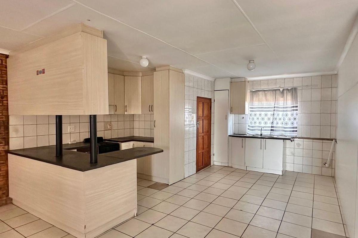 A spacious, empty kitchen featuring laminate cabinetry, a breakfast bar, tiled flooring, and a tiled splashback, offering a functional layout ready for modernization.