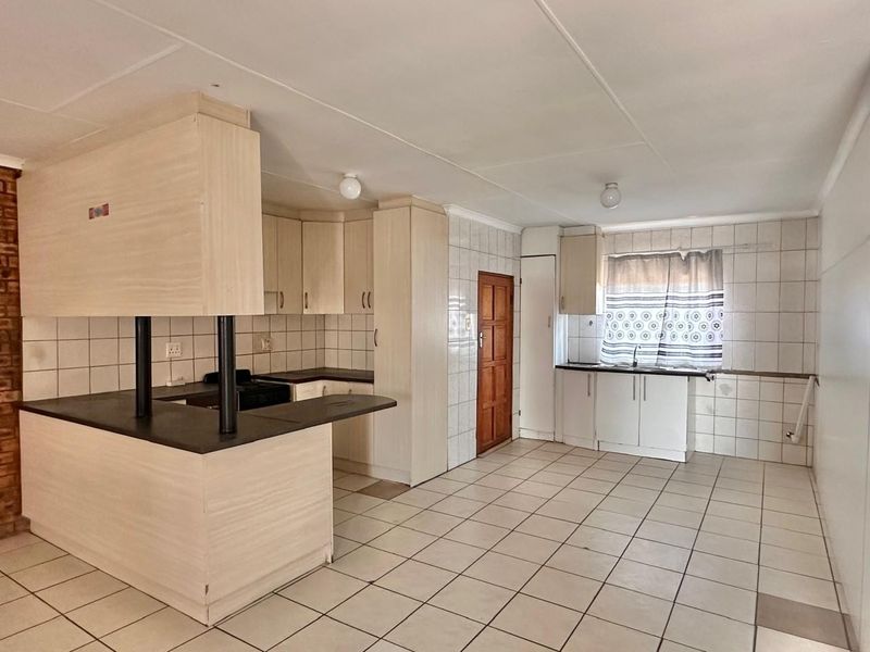 A spacious, empty kitchen featuring laminate cabinetry, a breakfast bar, tiled flooring, and a tiled splashback, offering a functional layout ready for modernization.
