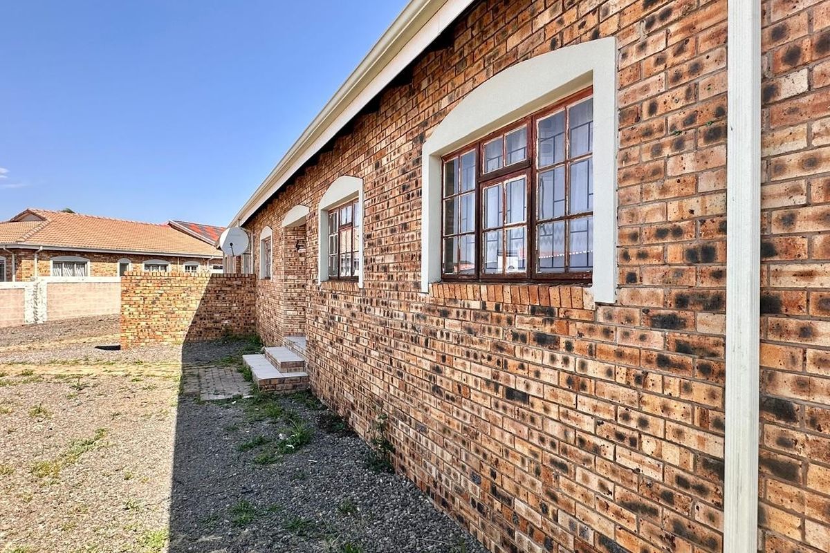 A side view of the townhouse featuring a face brick exterior, timber frame windows, and concrete steps leading to the entrance.