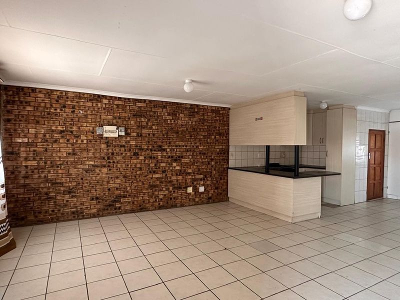 Open plan living area featuring an exposed brick wall, tiled flooring, and a functional kitchen with a breakfast bar and built-in cabinetry.