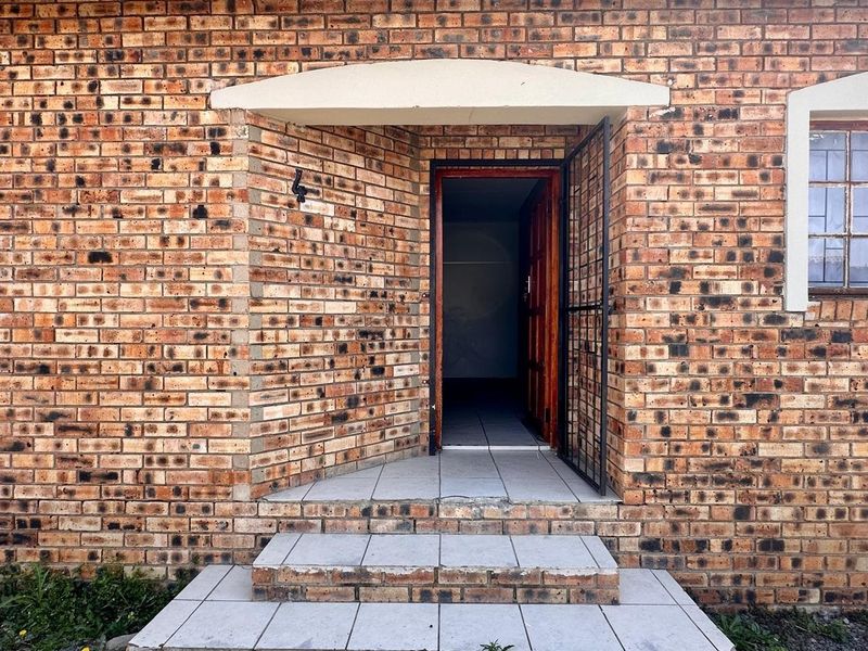 Front entrance of a townhouse featuring a face brick facade, security gate, and tiled steps leading to a timber front door.