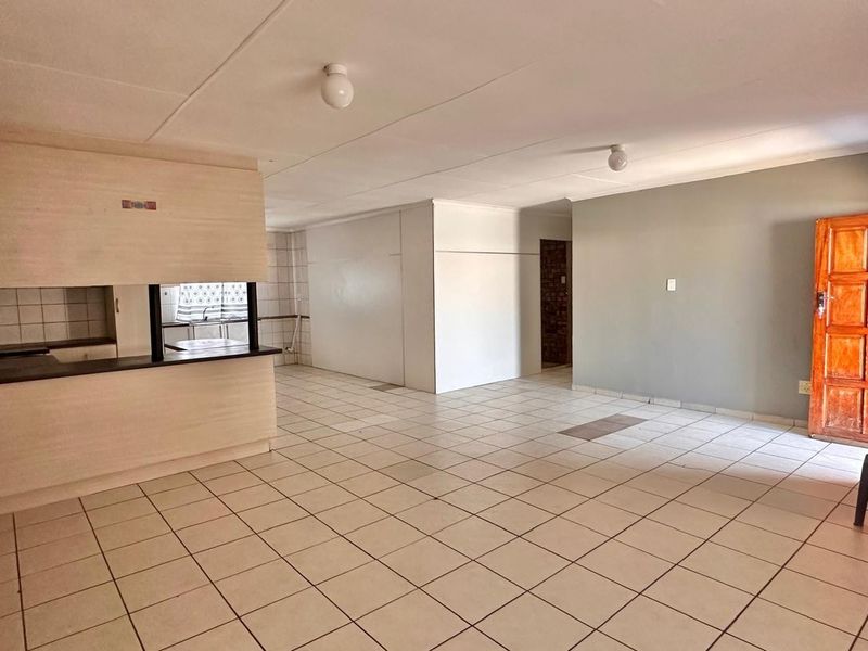 An open-plan living and kitchen area featuring tiled flooring, neutral walls, and built-in kitchen cabinetry, offering a blank canvas for renovation.