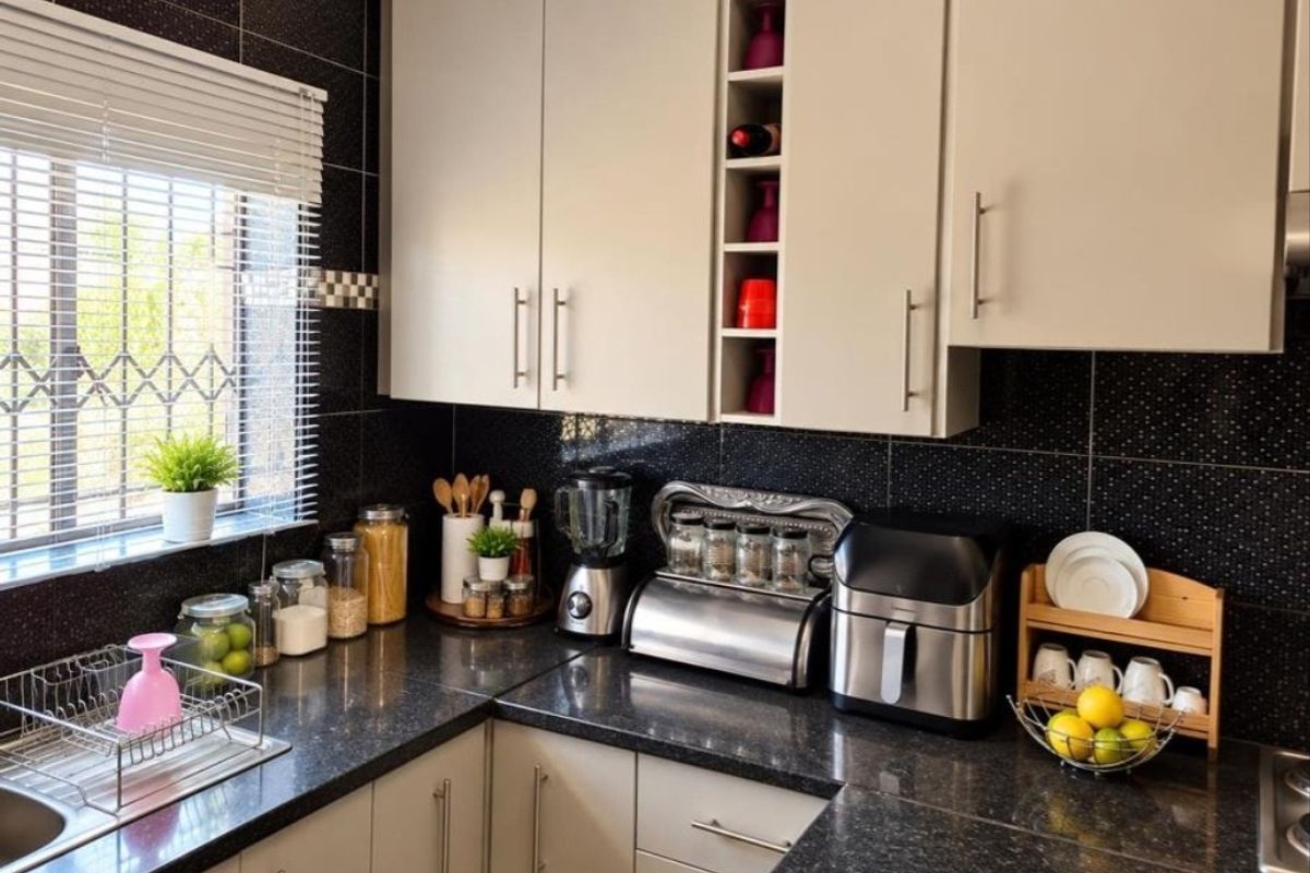 A well-maintained kitchen featuring dark granite countertops, light-toned cabinetry with integrated wine storage, and a contrasting black tiled backsplash.