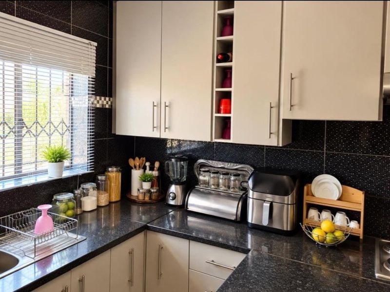 A well-maintained kitchen featuring dark granite countertops, light-toned cabinetry with integrated wine storage, and a contrasting black tiled backsplash.