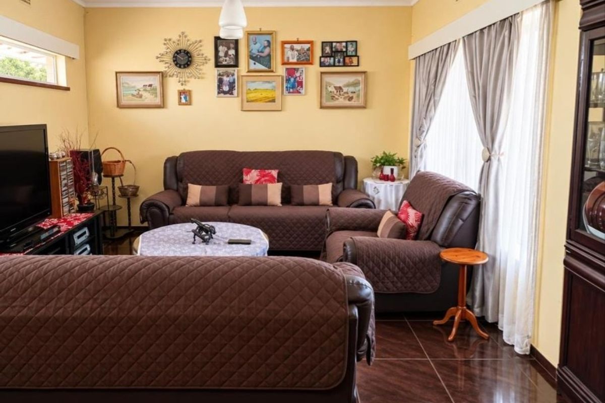 A comfortable living room featuring tiled flooring, neutral wall finishes, and large windows with curtain treatments, providing a functional and well-lit space.