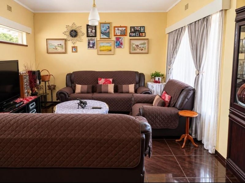 A comfortable living room featuring tiled flooring, neutral wall finishes, and large windows with curtain treatments, providing a functional and well-lit space.