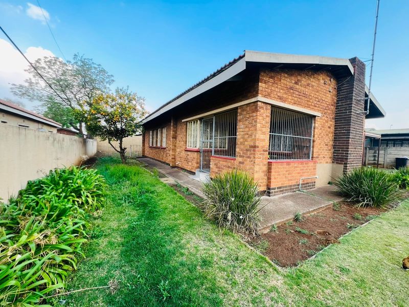 Rear view of a face brick house featuring a concrete apron, security bars on windows, and a private garden area.