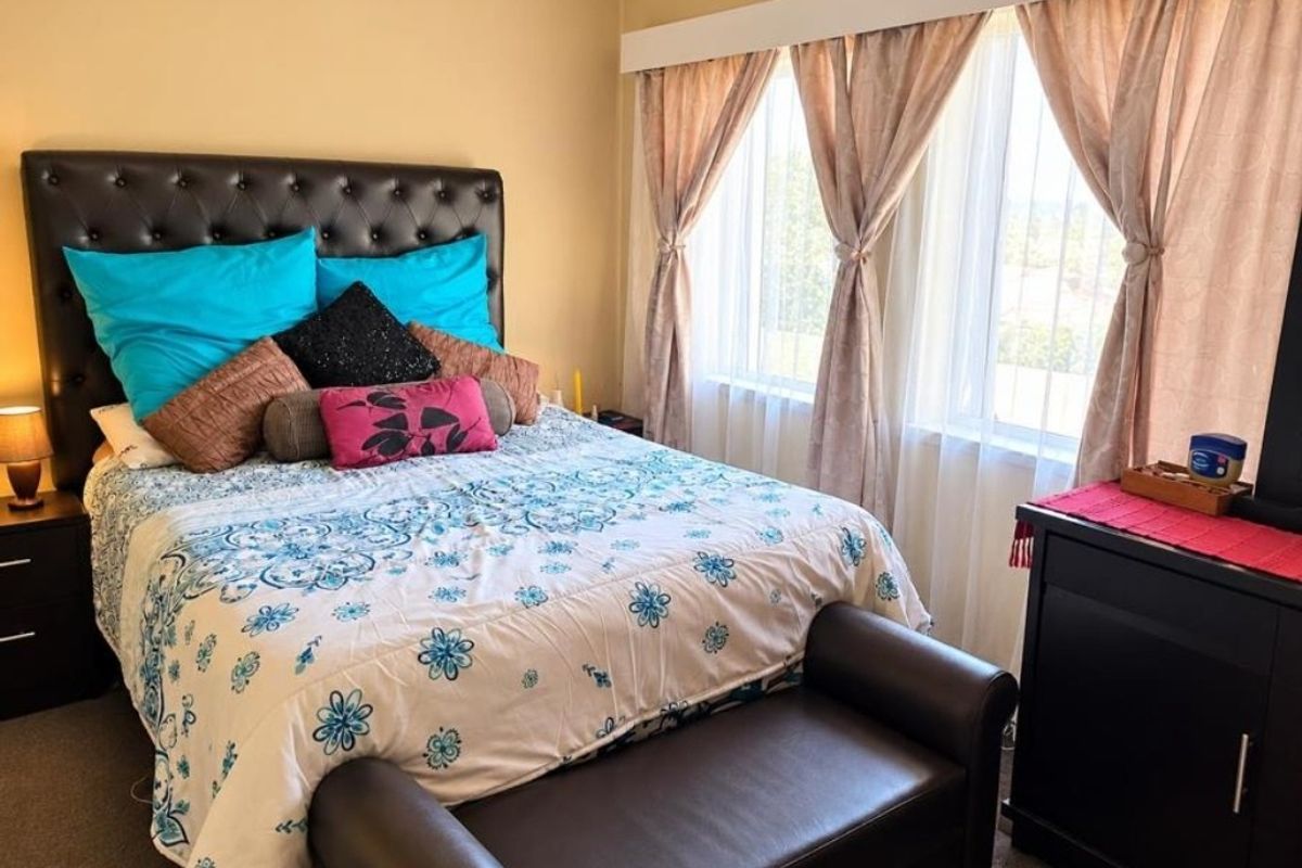 A well-lit bedroom featuring neutral wall tones, carpeted flooring, and a window fitted with a decorative pelmet and curtains.