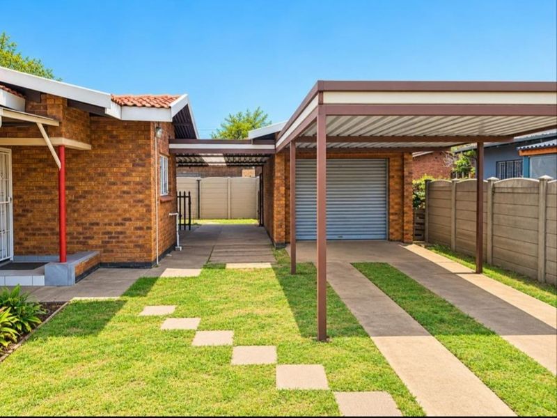 Front exterior view featuring a brick house, a covered carport, a single garage with a roller door, and a paved driveway with lawn sections.