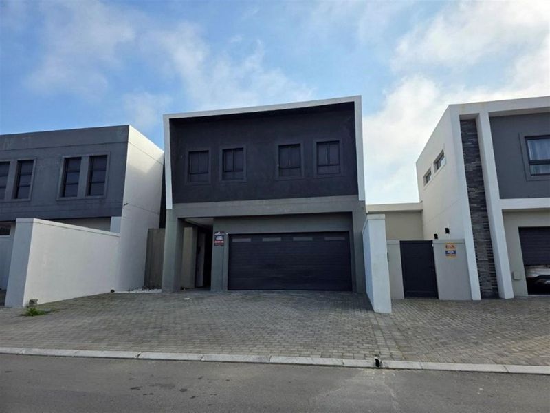 Modern double-story residential facade featuring a dark grey finish, integrated double garage, and paved driveway entrance.