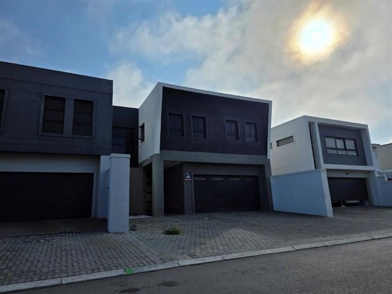 Modern multi-unit residential facade featuring contemporary dark and light exterior finishes, paved driveway access, and integrated double garages.