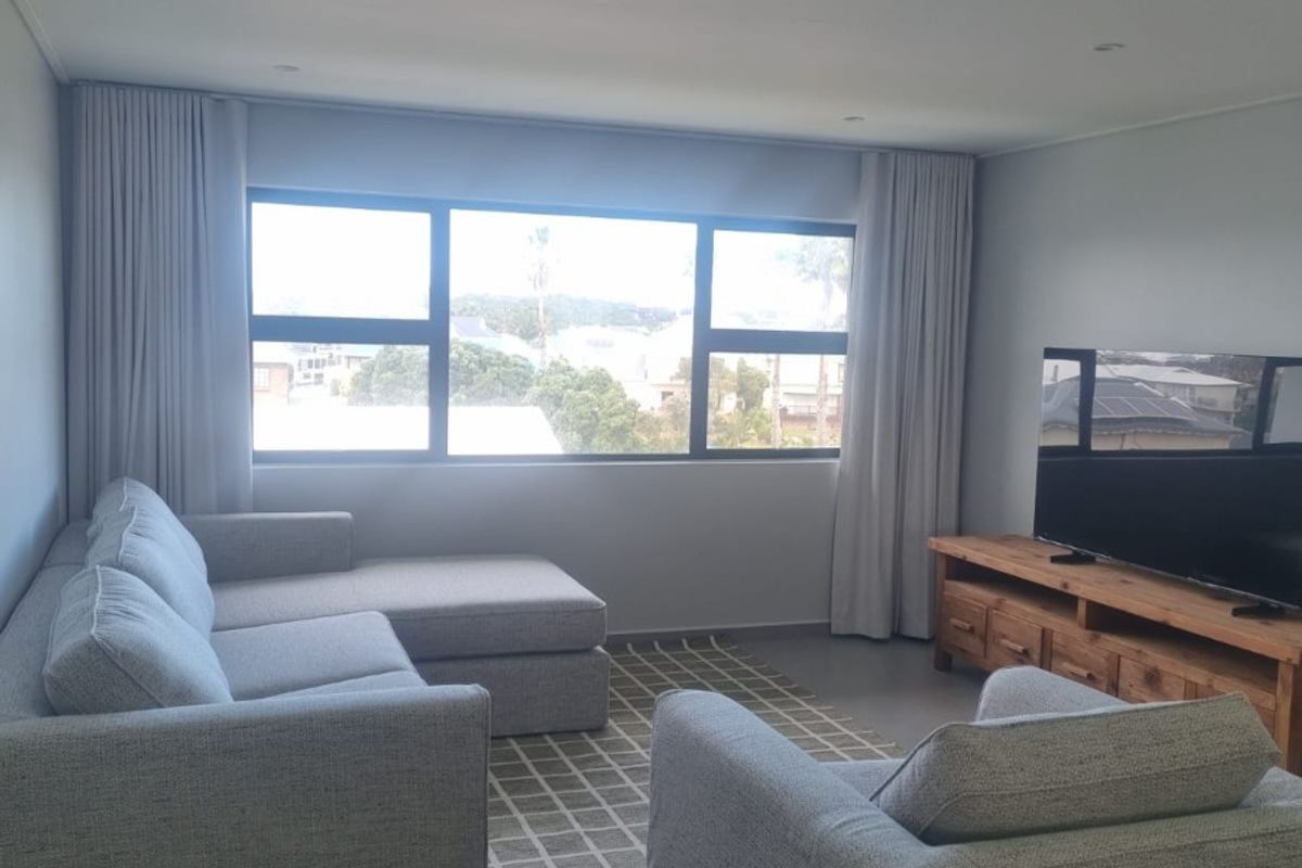 A bright and modern living room featuring large windows with curtain tracks, recessed downlighting, and neutral tiled flooring.