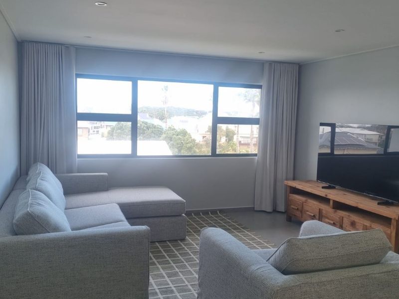 A bright and modern living room featuring large windows with curtain tracks, recessed downlighting, and neutral tiled flooring.