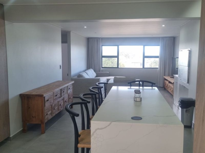 Spacious open-plan living and dining area featuring a modern stone kitchen island, recessed lighting, and large windows providing natural light.